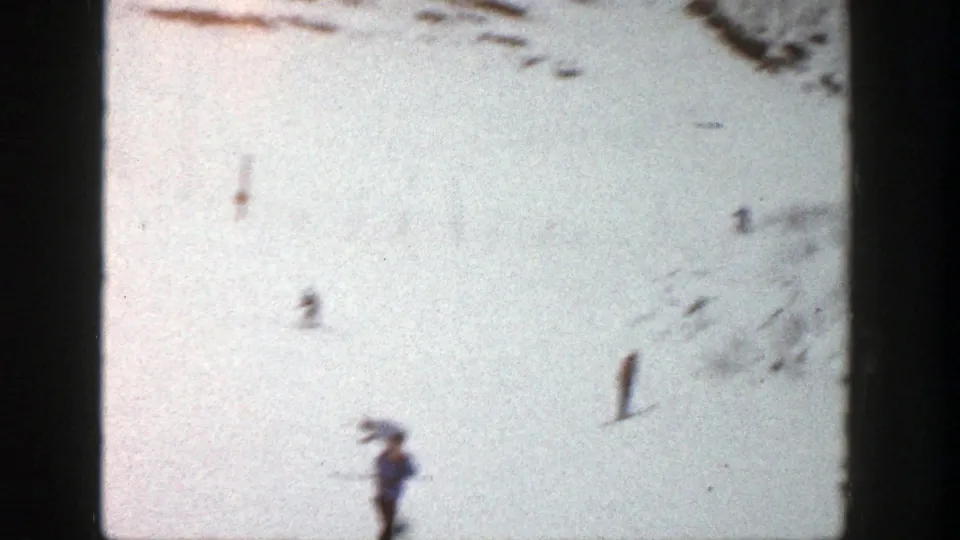 A skier passes near the lower left while smaller figures cross the snowy Aspen slope in grainy 8mm footage.