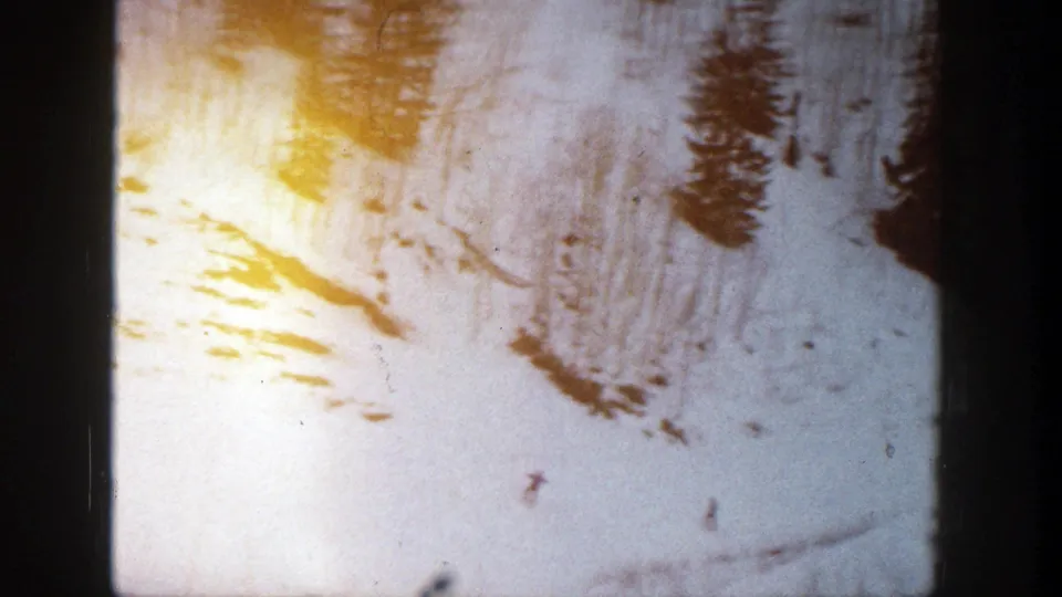 Aspen ski slope frame with evergreen clusters, distant skiers, visible snow tracks, and warm 8mm exposure variation.