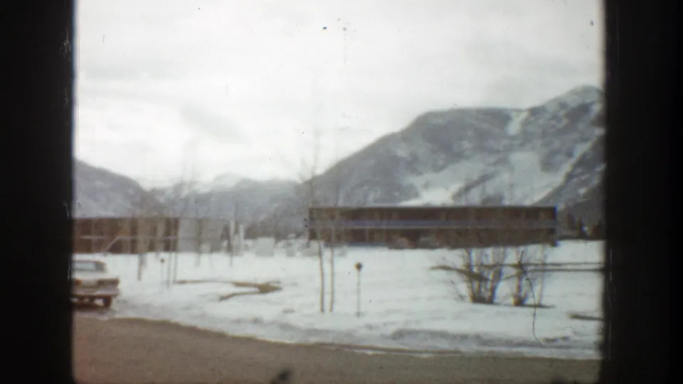 Aspen, Colorado winter resort view from 1961 with a partially visible car, snow, lodge, and mountains.