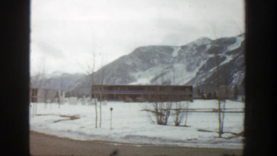 1961 Aspen resort scene showing snowy open grounds, a low lodge building, bare trees, and mountain slopes.