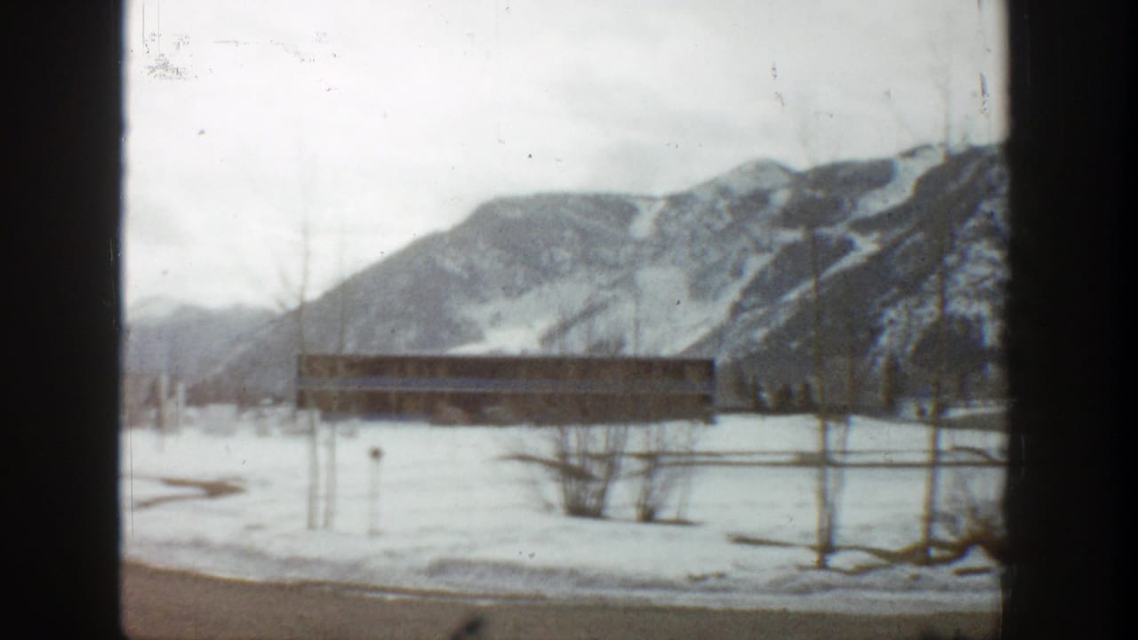 Snowy roadside view with a low building and mountains in the background.