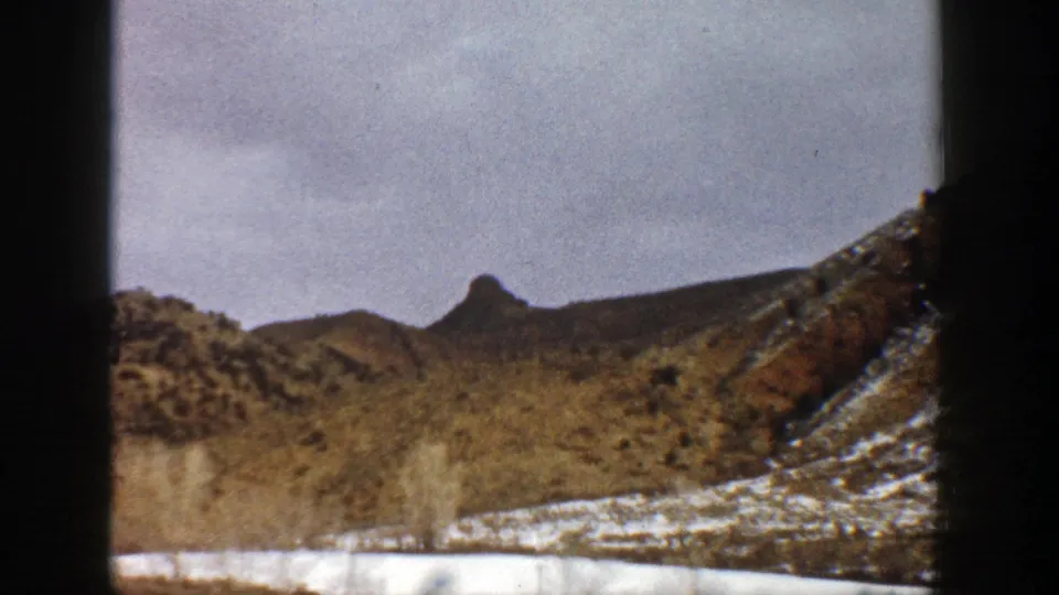 The clip shifts to a drier mountain view with scrub-covered slopes, snow patches, and a cloudy sky in 1961 Colorado home-movie footage.