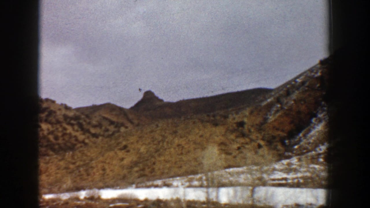 1961 Aspen-area mountain landscape with snow patches, scrubby slopes, and dark vertical frame edges from the 8mm scan.