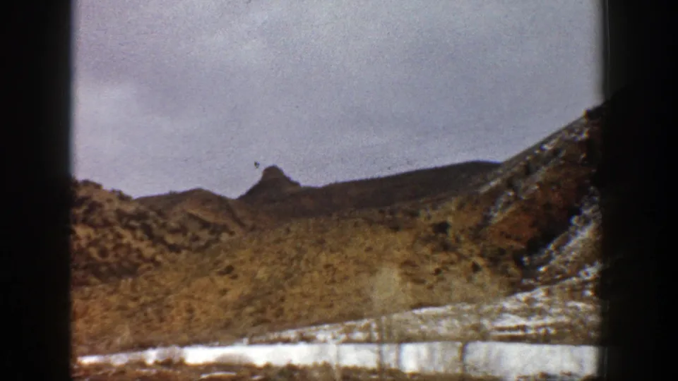 1961 Aspen-area mountain landscape with snow patches, scrubby slopes, and dark vertical frame edges from the 8mm scan.