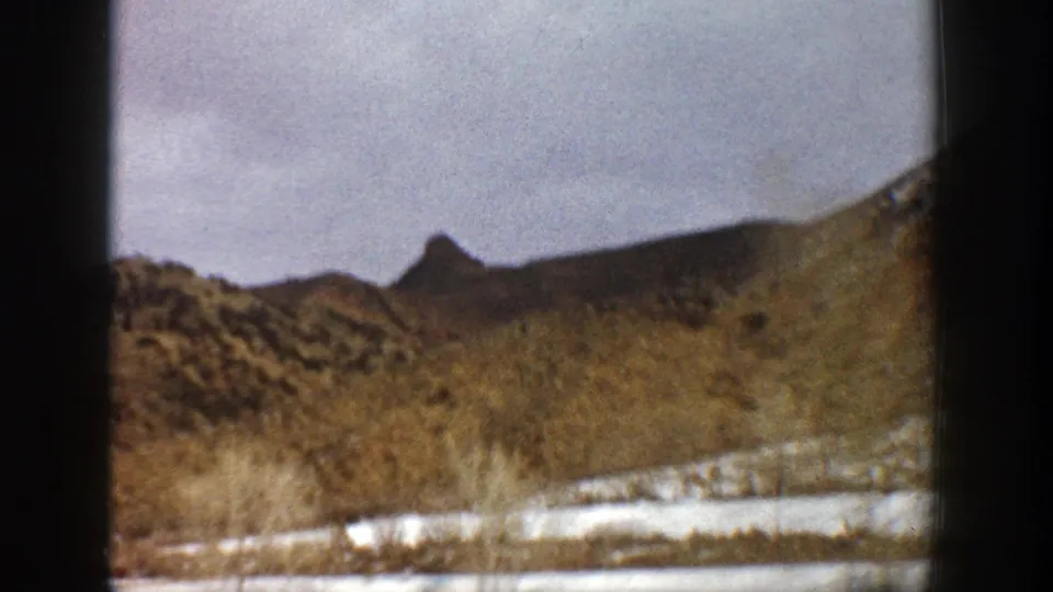 Roadside Aspen, Colorado landscape on 8mm film, with a rocky hill, snow on the ground, and dark gate or vehicle-edge framing.