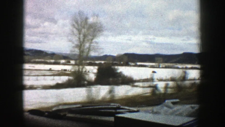 1961 Aspen-area winter landscape seen from a moving vehicle, with snow-covered fields, bare trees, and distant hills.