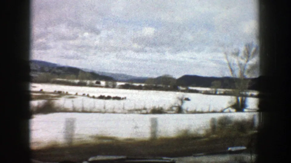 Snow-covered Aspen-area fields and distant hills appear beyond the car window frame in this 1961 8mm travel view.