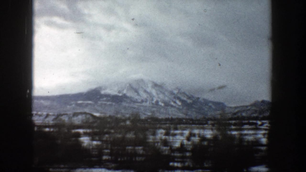 Snowy mountain range under cloudy sky with dark trees and film-frame borders.