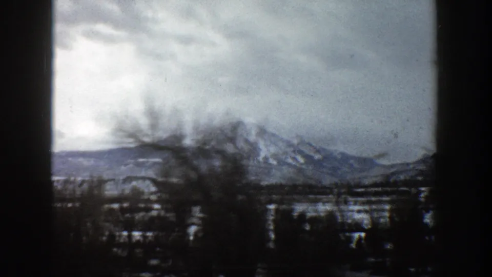 1961 Aspen, Colorado view of a snowy mountain partly obscured by foreground trees and passing motion blur.