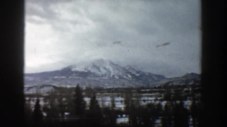 1961 Aspen, Colorado landscape view showing the mountain range across a snowy valley with trees in the foreground.