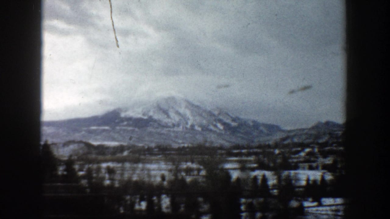 1961 Aspen, Colorado footage showing a snowy mountain landscape under a muted gray sky, framed by dark 8mm gate edges.