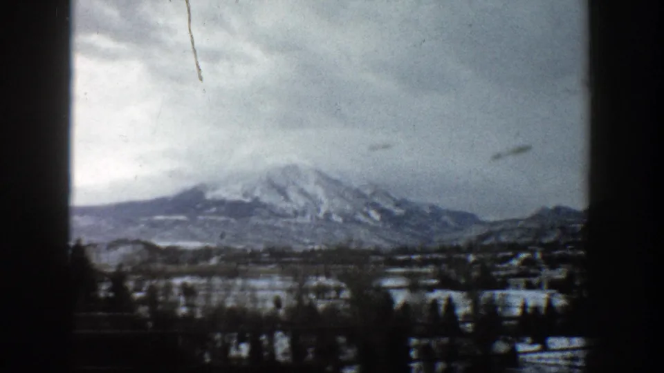 1961 Aspen, Colorado footage showing a snowy mountain landscape under a muted gray sky, framed by dark 8mm gate edges.
