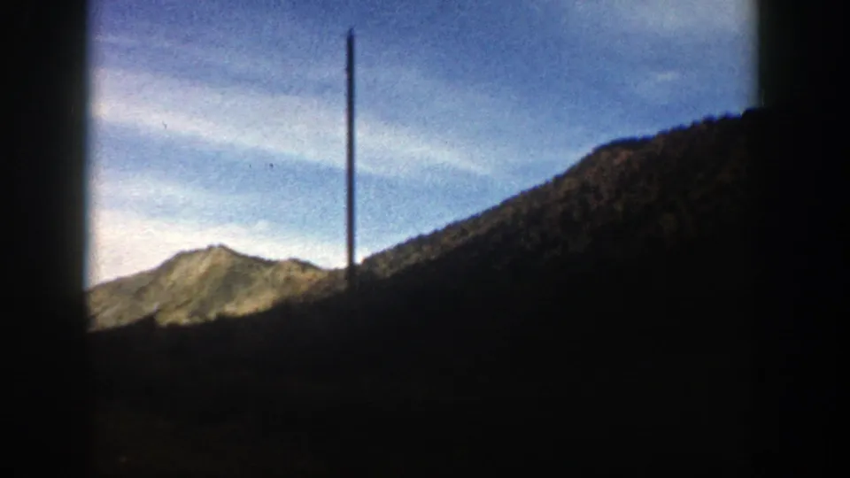 1961 Aspen, Colorado footage with sunlit summer ridges, a dark hillside, blue sky, and a tall pole visible near the ridgeline.