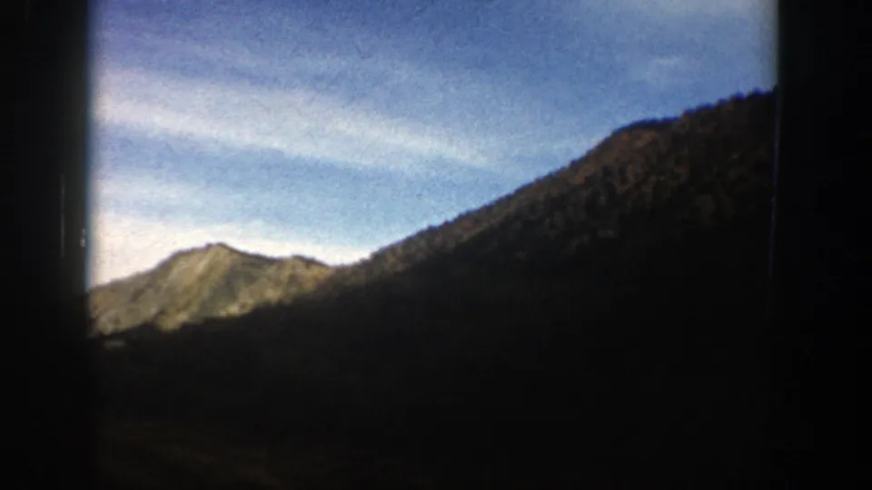 1961 Aspen, Colorado footage showing a bright mountain ridge beside a shadowed slope, with soft 8mm color and dark borders.