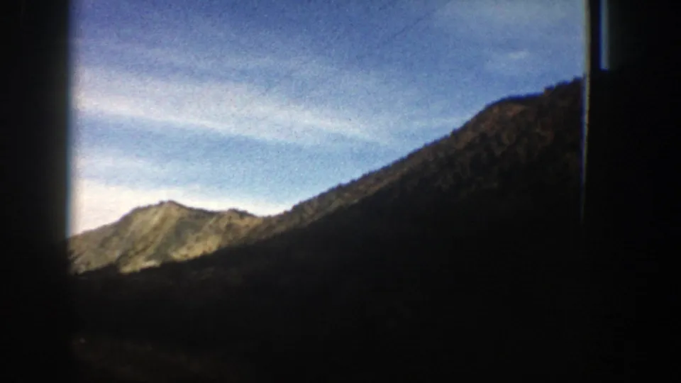 1961 Aspen, Colorado footage holding on a sunlit ridge and dark mountain slope beneath a pale blue sky, with visible home-movie framing.