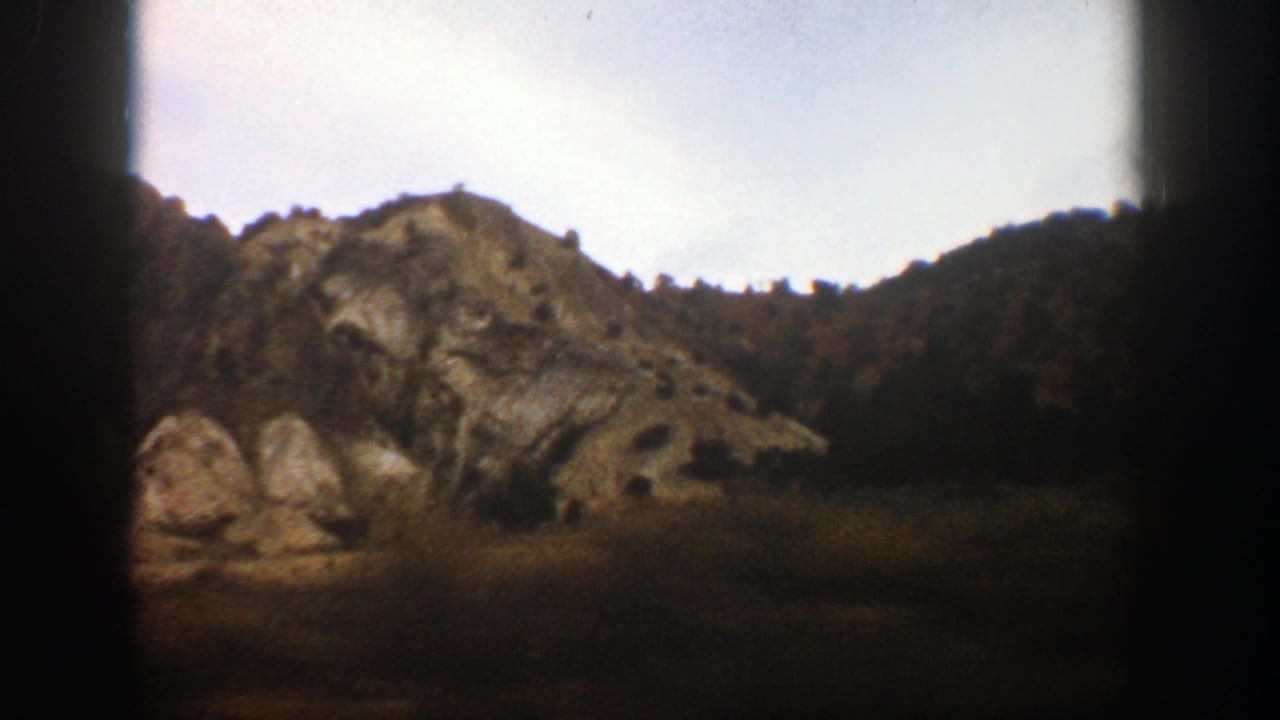 1961 Aspen-area mountain hillside seen from a moving car, with dark 8mm frame edges and soft focus.
