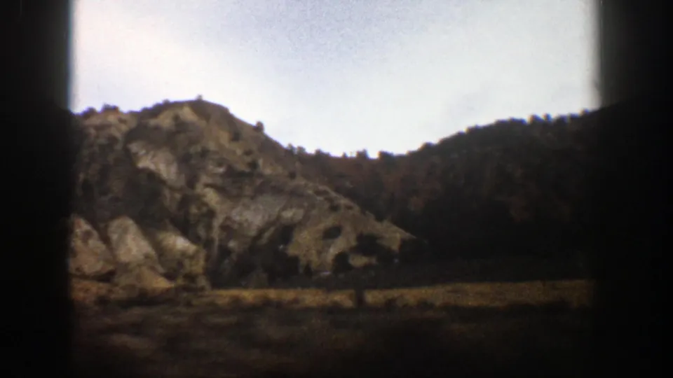 Mountain slope near Aspen, Colorado, viewed from a moving car in 1961 8mm footage, with a dark window edge at center.