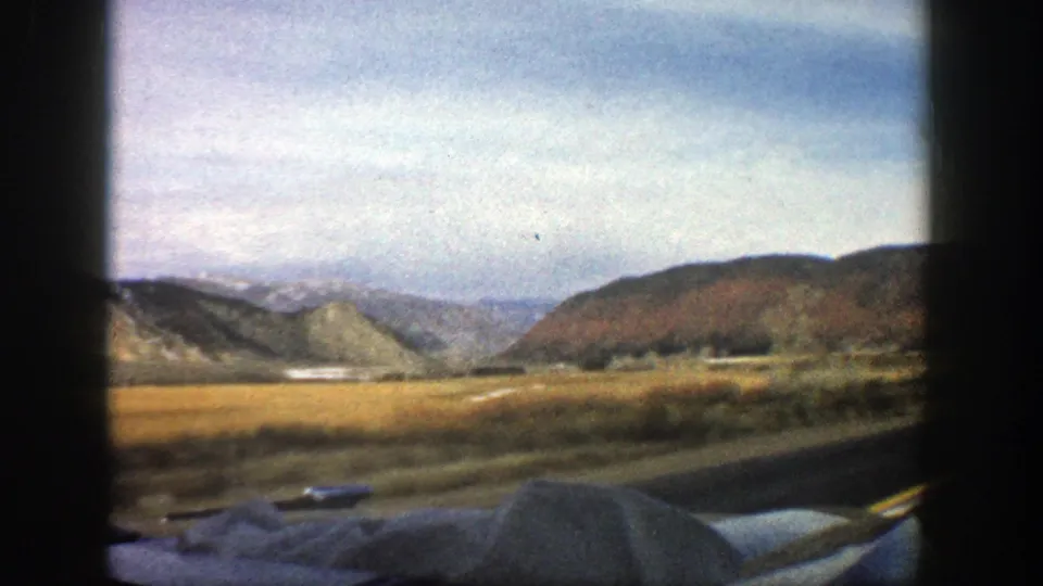 Aspen-area valley landscape in 1961 home-movie footage, with distant hills, open fields, and part of the car visible below.