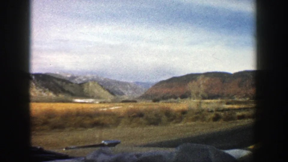 Roadside valley near Aspen, Colorado, filmed from a moving car in 1961, with hills, fields, and 8mm border shadows visible.