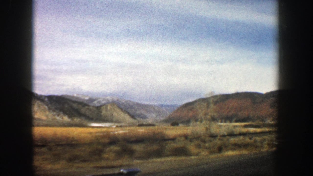 1961 Aspen, Colorado home-movie frame looking from a moving vehicle across sagebrush flats toward low hills and distant mountains.