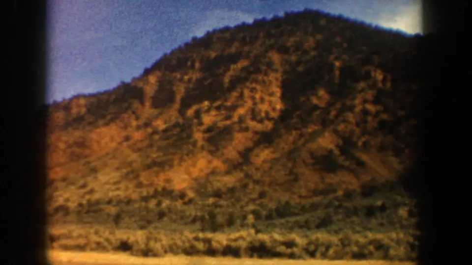 1961 Aspen, Colorado home-movie frame with a closer view of a dry hillside, scrub vegetation, and shadowed mountain slope.