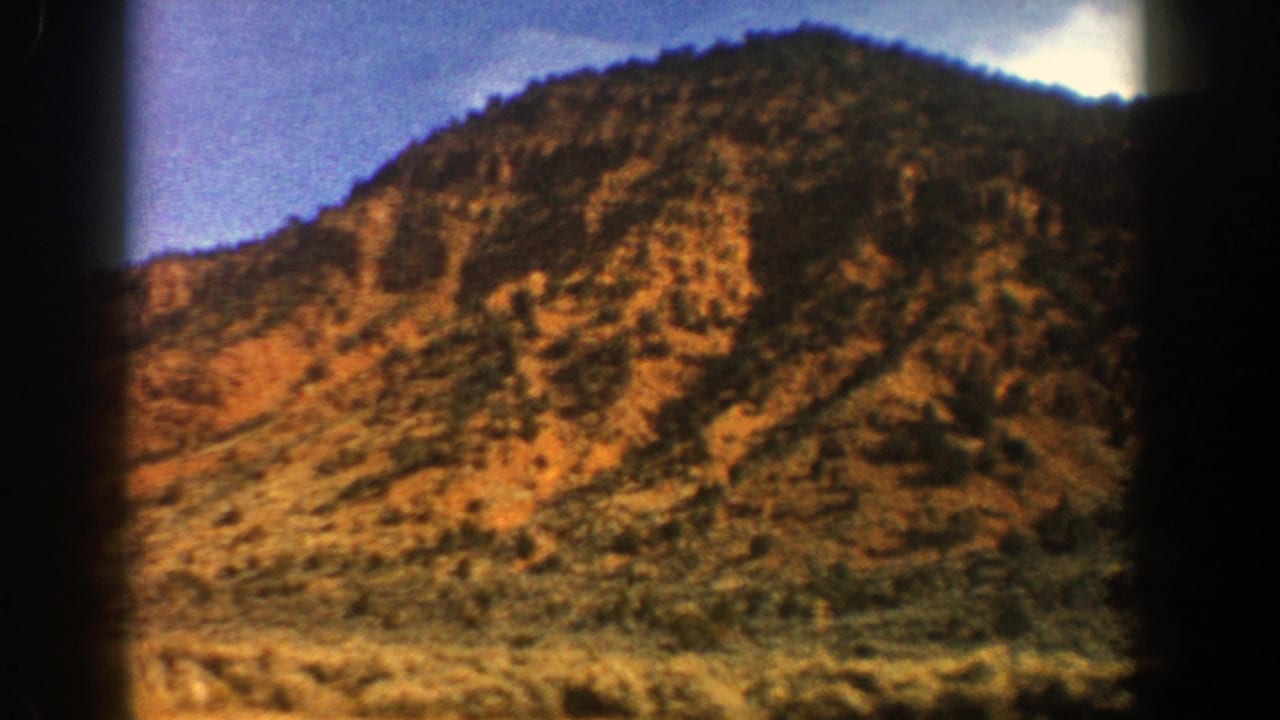 Rocky tree-covered mountain slope under blue sky with black film edges.