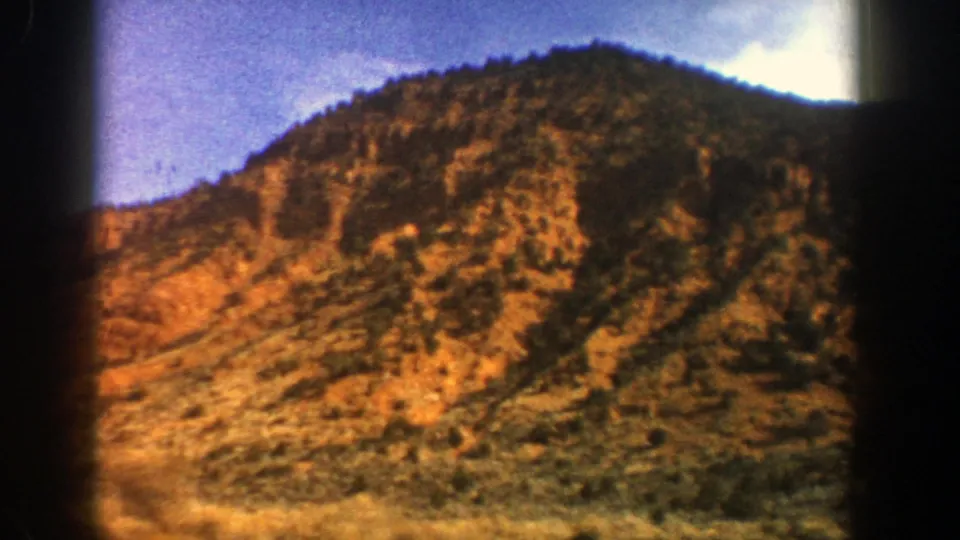 Vintage 8mm frame of an arid mountain face near Aspen, Colorado, with scattered trees, warm rock tones, and blue sky.