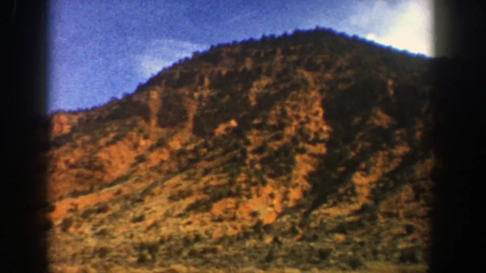 1961 home-movie frame showing a dry, wooded mountain slope in the Aspen, Colorado area, softened by grain and warm color.