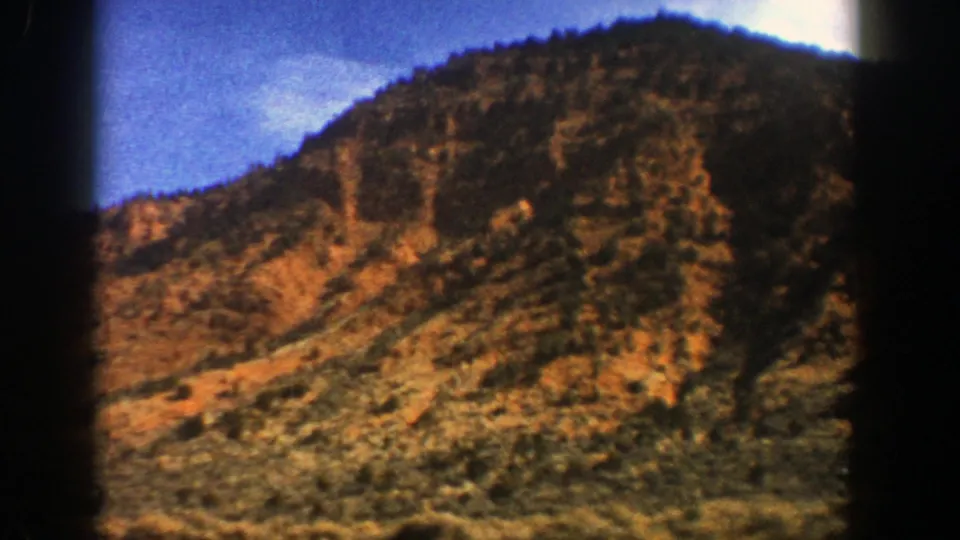 8mm frame from 1961 near Aspen, Colorado, showing a tree-covered rocky mountain slope with scrub vegetation and dark gate edges.