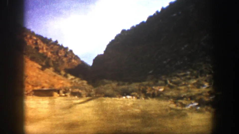 1961 8mm view near Aspen, Colorado, showing a rugged valley, sparse vegetation, and a road glimpsed from a moving vehicle.