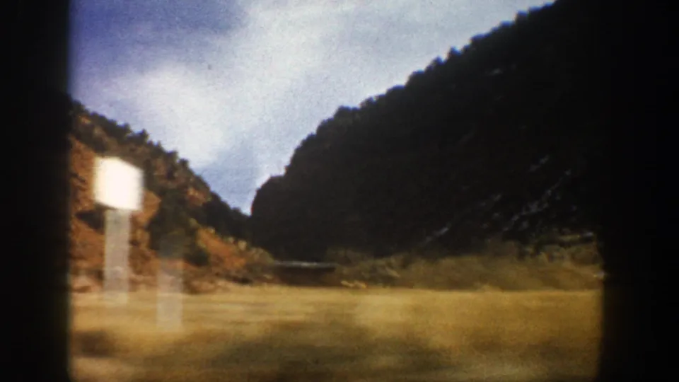 Blurred roadside sign appears beside a grassy mountain road in the 1961 Aspen, Colorado home-movie footage.