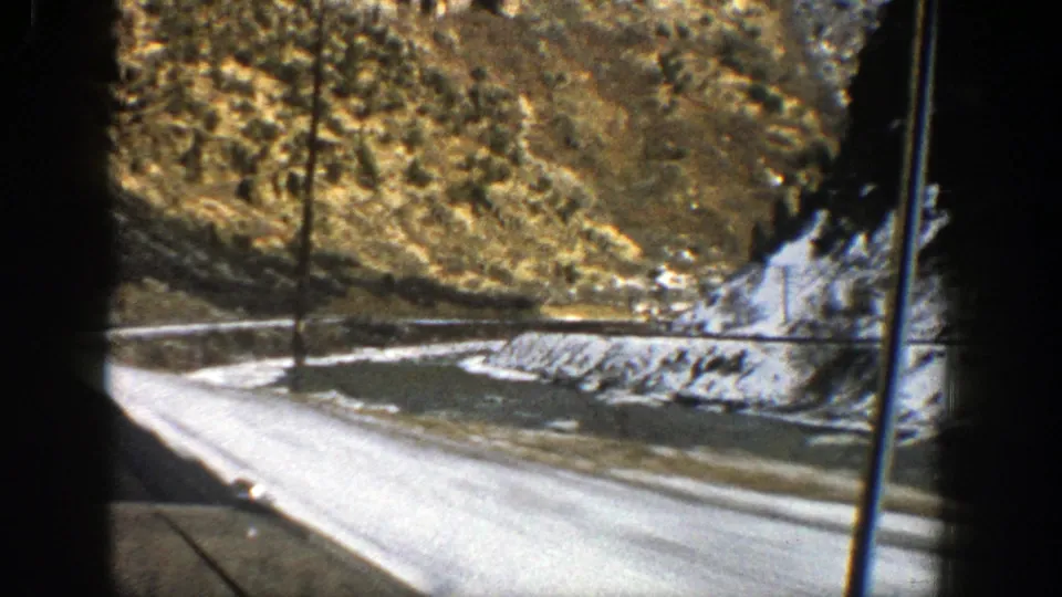 Aspen-area 8mm frame from 1961 showing a snow-edged mountain road and rocky slope through the vertical framing of a car window.
