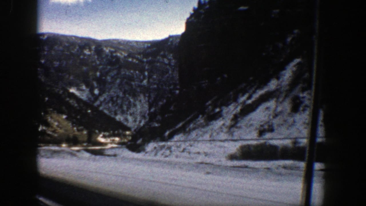 1961 Aspen-area 8mm frame showing a snowy canyon, distant ridges, and a river or road corridor seen from a moving vehicle.