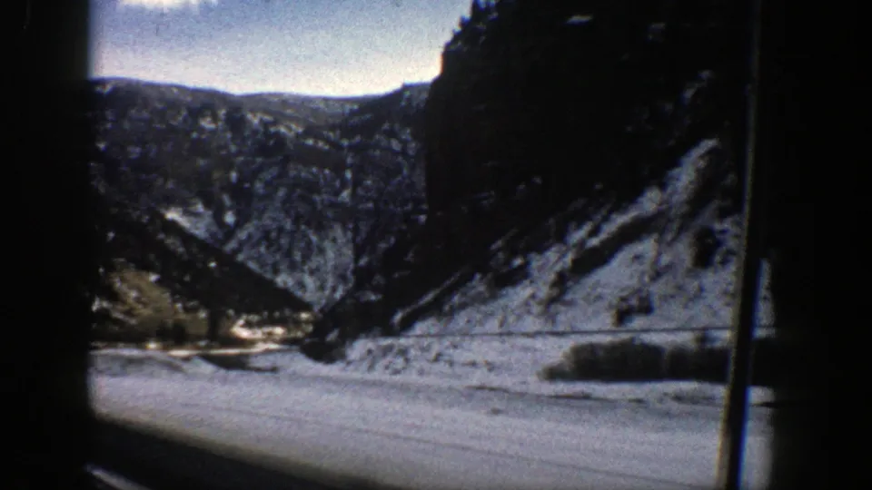 1961 Aspen-area 8mm frame showing a snowy canyon, distant ridges, and a river or road corridor seen from a moving vehicle.