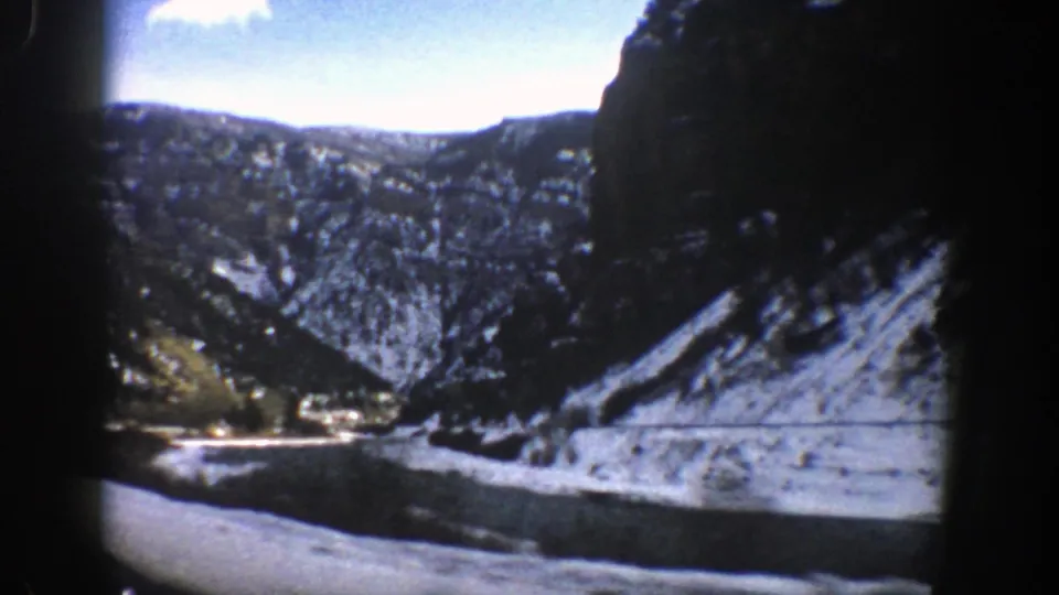 1961 Aspen, Colorado frame with a river at the canyon base, snowy slopes, and dark in-camera framing from travel footage.