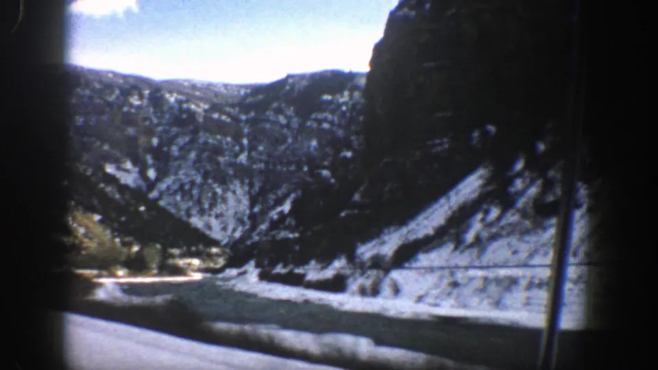End frame from 1961 Aspen-area 8mm footage showing a snowy river canyon and wooded ridges through a moving vehicle window.