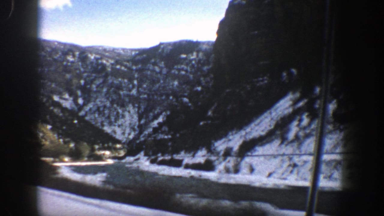 Snow-dusted mountain road and river seen through dark film-frame edges.