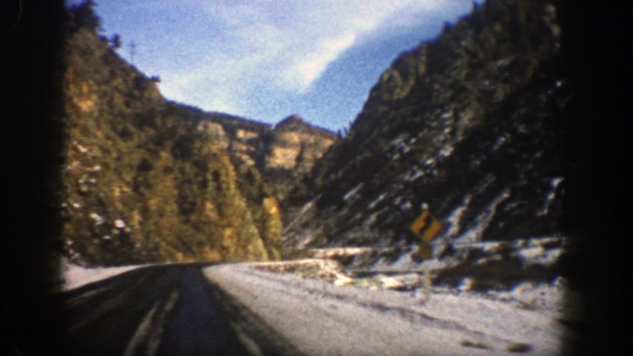 Curving paved road beside snowy mountain slopes and evergreen trees.