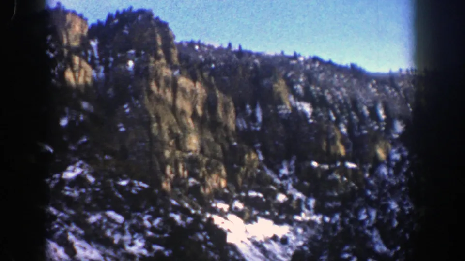 1961 Aspen, Colorado home-movie view of a steep rocky slope with evergreen forest and lingering snow below.