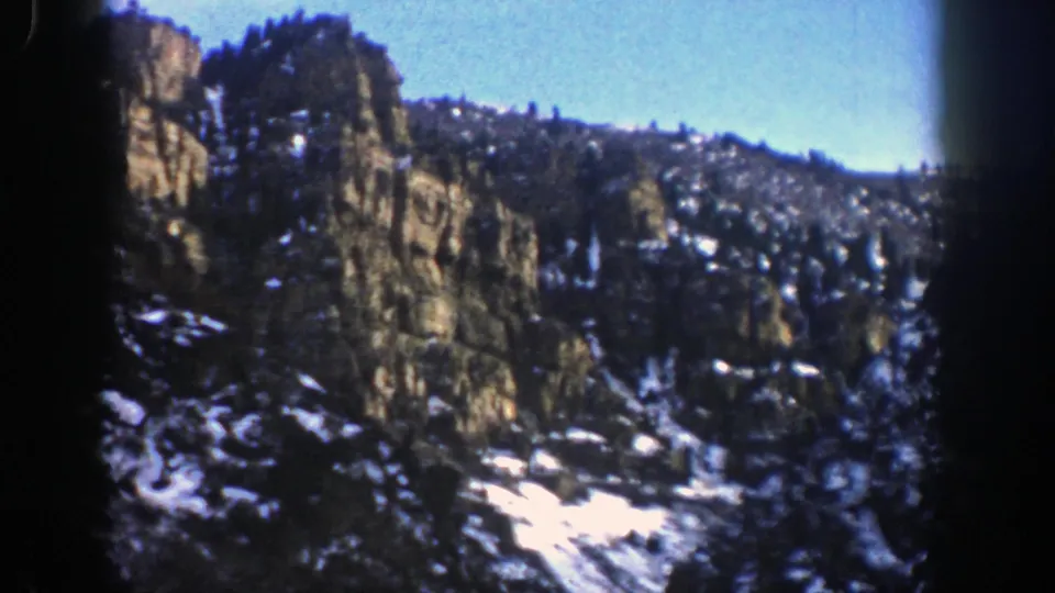 1961 Aspen, Colorado frame showing a rocky outcrop, evergreen-covered slope, and bright snow patches in a mountain scene.