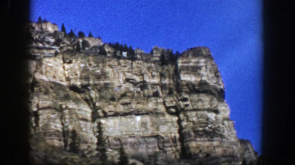 1961 Aspen, Colorado home-movie still with a close, slightly soft view of a rock face below vivid blue sky.