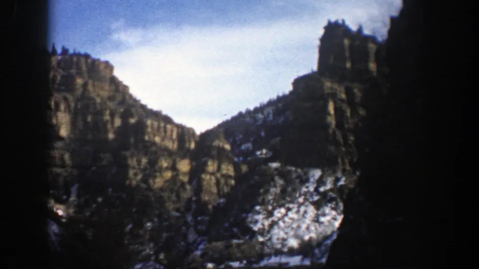 Aspen, Colorado mountain view on 8mm film, with steep rock faces, snow-dusted slopes, and dark borders from the filmed frame.