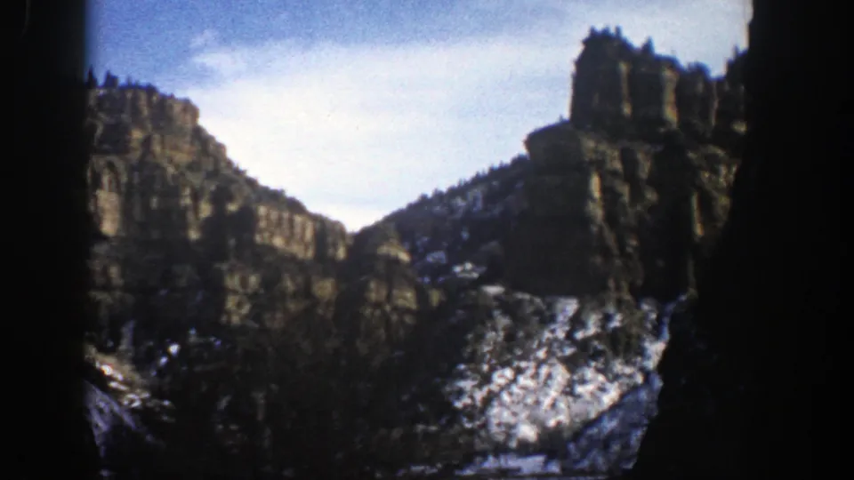 Vintage 1961 home-movie view near Aspen showing rugged cliffs, patchy snow, bare trees, and soft color film grain.