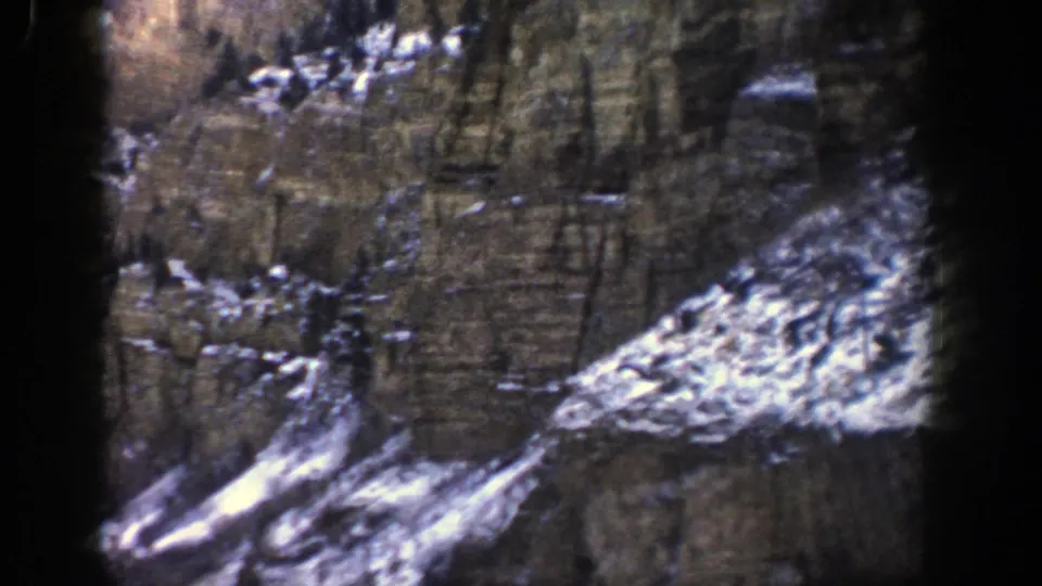 Layered mountain cliffs and snow-covered ledges appear in this 1961 8mm Aspen road-trip frame.