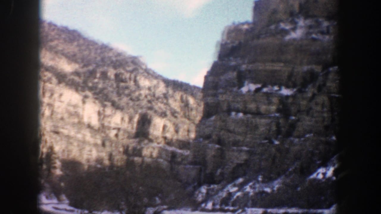 1961 Aspen, Colorado 8mm frame showing a snowy canyon road approaching tall rock cliffs and evergreen slopes.