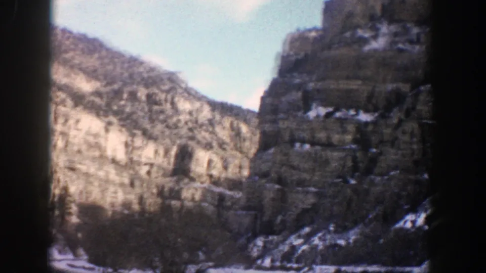 1961 Aspen, Colorado 8mm frame showing a snowy canyon road approaching tall rock cliffs and evergreen slopes.