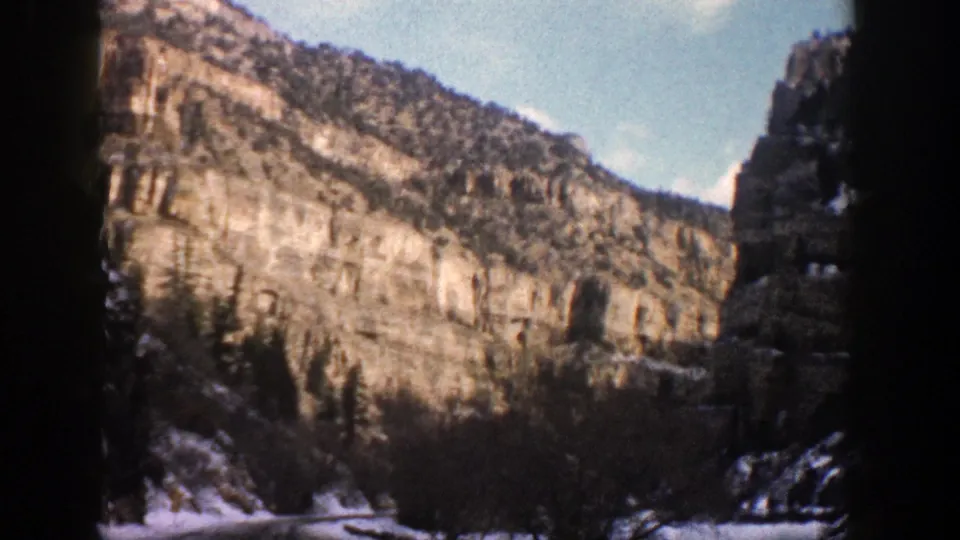 A moving 8mm view of Aspen-area canyon cliffs, evergreen trees, and snow along the lower slope.
