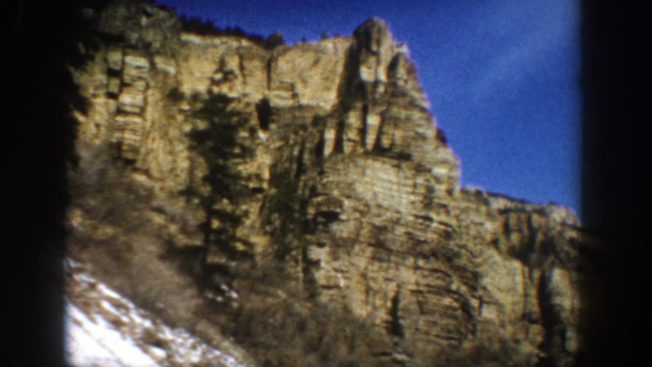 Layered tan cliff face above snow-dusted slope under a deep blue sky.