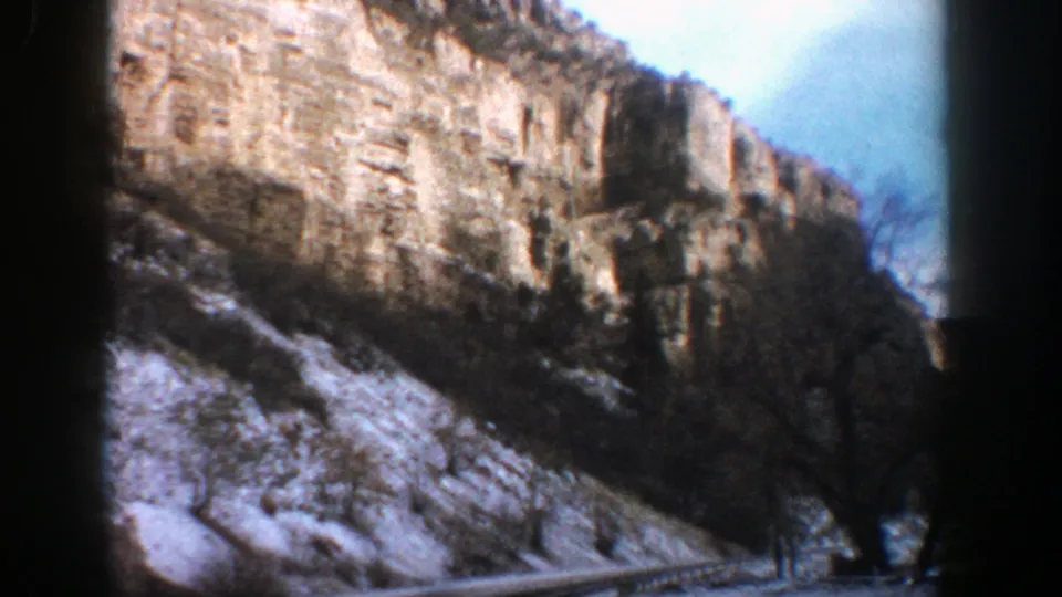 1961 Aspen, Colorado 8mm frame showing a long rock wall, snow-covered ground, sparse trees, and a pale winter sky.