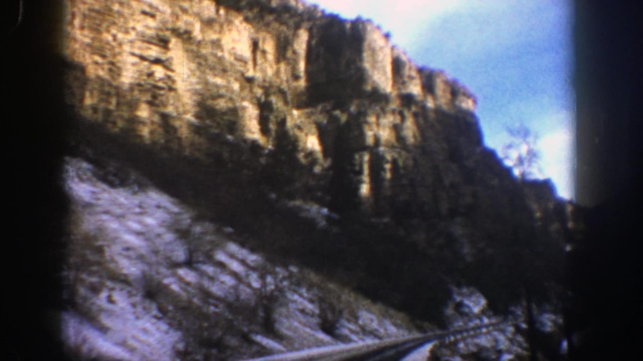 Rocky canyon wall above a curving road with snow on the slope.
